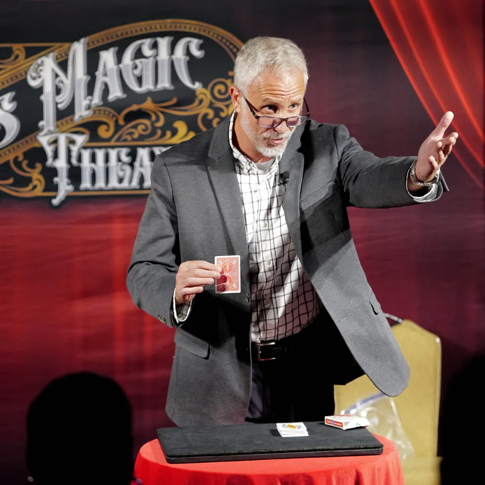 Mike Stringer showing a card to the audience beside a red table